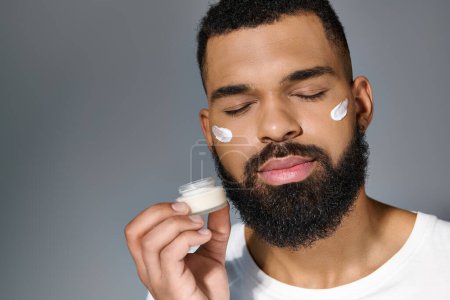 A handsome young man with a beard applying cream to his face.