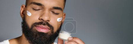 Téléchargez les photos : Africain américain beau jeune homme qui applique de la crème sur son visage. - en image libre de droit