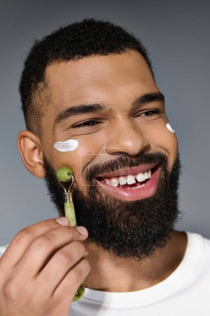 Africain américain jeune homme avec de la crème sur le visage à l'aide de rouleau de visage.