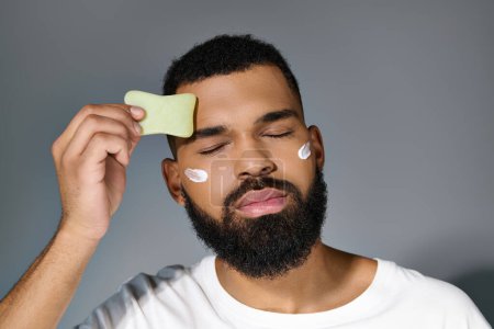 African american stylish man with cream on his face using face roller.
