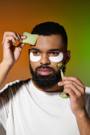 Hombre barbudo afroamericano usando parches para los ojos y rodillo facial.