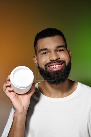 Handsome young man with a beard holding a container of cream.