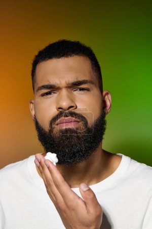 A stylish man with a beard carefully holds his skincare product.