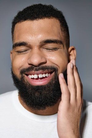 Handsome man with beard smiles while touching his face.