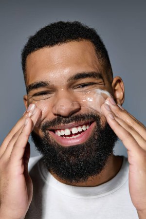 A bearded man happily applying cream on his face.