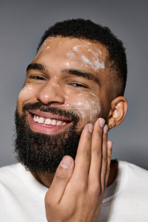 Photo for Appealing man with beard in white t-shirt, focusing on skincare routine. - Royalty Free Image