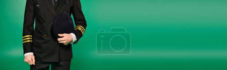 Photo for Handsome pilot in black suit and tie striking a pose against a vibrant green background. - Royalty Free Image