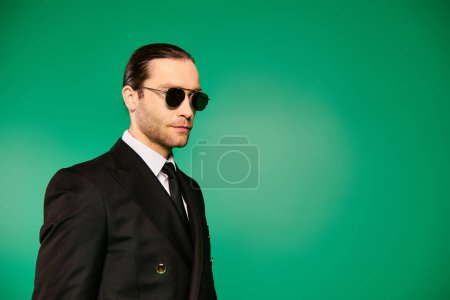 Schöner Pilot in schwarzem Anzug und Sonnenbrille posiert vor leuchtend grünem Hintergrund.
