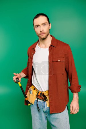 Ein gutaussehender männlicher Arbeiter in Uniform mit Werkzeuggürtel vor grünem Hintergrund.