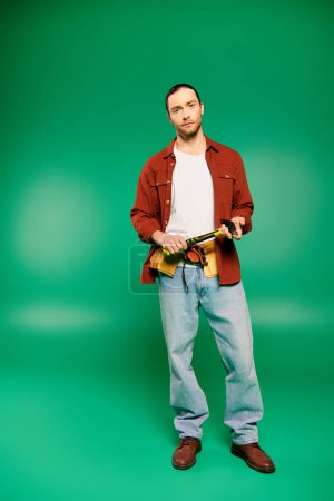 Handsome male worker in uniform with tools posing on green backdrop.