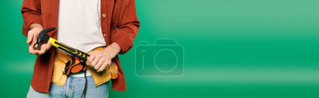 Photo for A handsome male worker holds a tools in his hands against a green backdrop. - Royalty Free Image