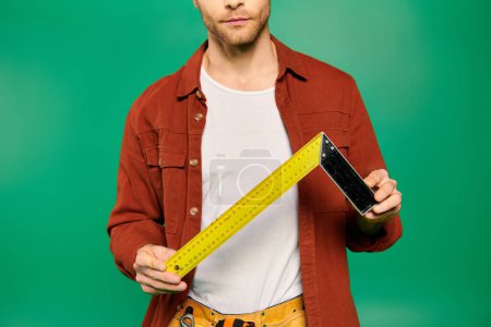 Un trabajador masculino guapo de uniforme sostiene una cinta métrica sobre un fondo verde.
