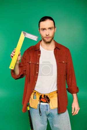 Handsome male worker in uniform holding a large yellow measuring tape against a green backdrop.