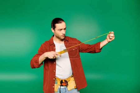 Téléchargez les photos : A man in a red shirt confidently holds a measuring tape. - en image libre de droit