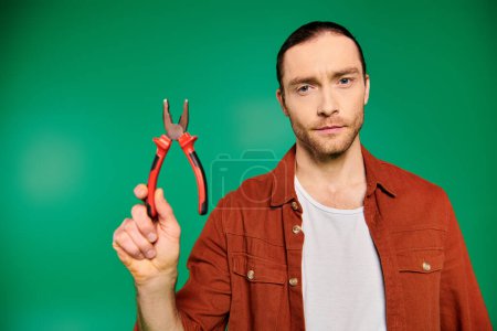 Handsome worker holding scissors in hand on green backdrop.