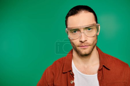 Téléchargez les photos : Beau travailleur masculin en uniforme et lunettes, posant avec des outils sur un fond vert vibrant. - en image libre de droit