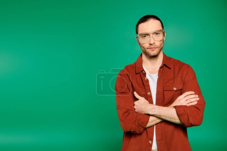 Photo for Handsome male worker in uniform with tools, standing with crossed arms against a green backdrop. - Royalty Free Image