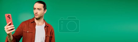 Photo for A handsome male worker in uniform using a cell phone on a vibrant green backdrop. - Royalty Free Image