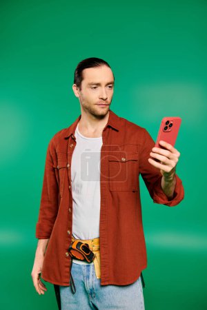 A man in a uniform holds a cell phone against a vibrant green backdrop.