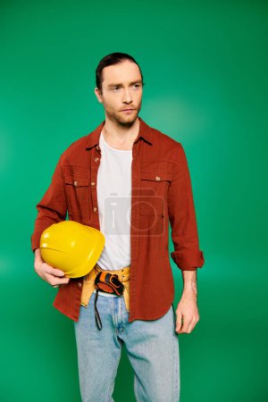 Handsome worker holding a hard hat and yellow hard hat on green backdrop.