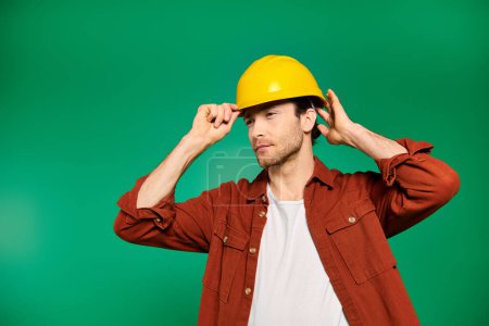 Foto de A handsome male worker in uniform striking a pose on green backdrop with yellow hard hat. - Imagen libre de derechos