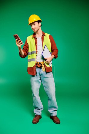 Ein gutaussehender männlicher Arbeiter in gelber Warnweste hält selbstbewusst ein Handy in der Hand.