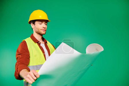 Photo for A handsome man in a hard hat holds a blueprint confidently. - Royalty Free Image