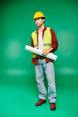 Un trabajador guapo de uniforme sostiene un papel enrollado sobre un fondo verde.