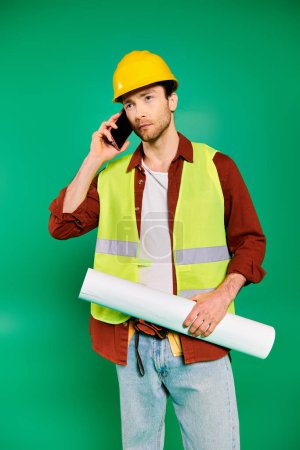Handsome male construction worker in uniform using a cellphone on a green backdrop.