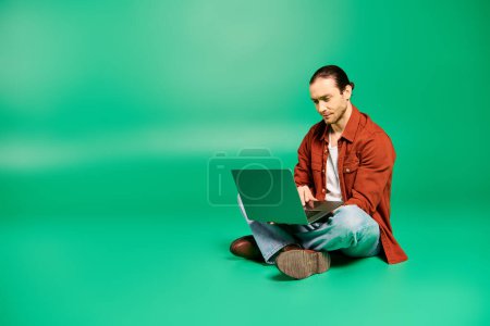 Photo for A man in uniform seated on floor, concentrated on laptop. - Royalty Free Image