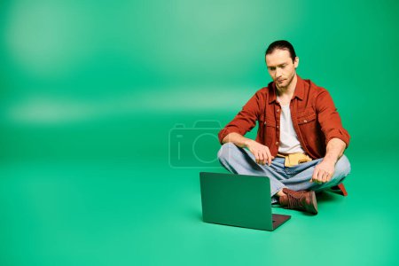 Photo for A man in a uniform sits on the floor working on a laptop. - Royalty Free Image