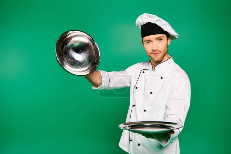 Ein gutaussehender männlicher Koch in weißem Gewand hält einen silbrig glänzenden Teller in der Hand.