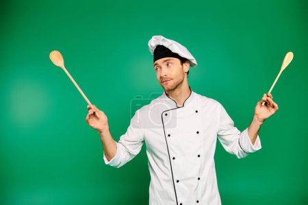 Guapo chef en uniforme blanco sosteniendo dos cucharas de madera.