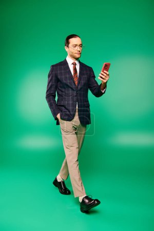 A handsome businessman in a chic suit and tie holding a cell phone against a green backdrop.