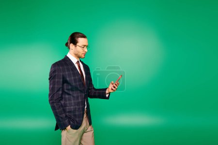 Photo for A handsome businessman in a chic suit holding a cell phone in front of a green screen. - Royalty Free Image