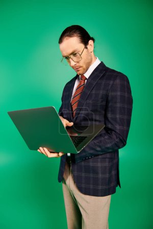 A businessman in a chic suit and tie diligently works on a laptop against a green backdrop.