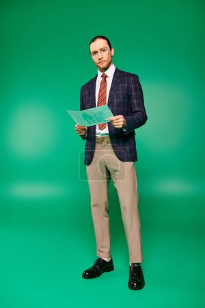 Photo for Handsome businessman in suit presenting paper against green backdrop. - Royalty Free Image
