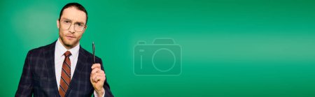 Téléchargez les photos : Un homme d'affaires élégant en costume chic tenant un stylo sur une toile de fond verte. - en image libre de droit
