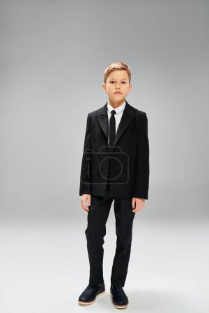Preadolescent boy in sharp suit and tie on a gray backdrop.