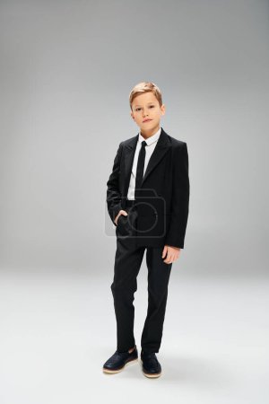 A preadolescent boy in a suit and tie standing against a gray backdrop.