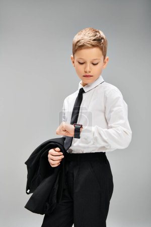 Adorable preadolescent boy in white shirt and black tie on gray backdrop, exuding elegance.