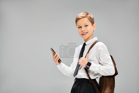 Little boy in white shirt, tie, holding cell phone.
