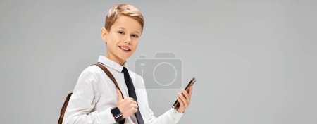 Preadolescent boy in white shirt and tie holding a cell phone, portraying a business concept.