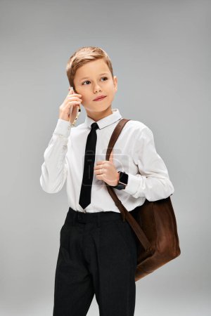 Frühpubertärer Junge in weißem Hemd und Krawatte vor grauem Hintergrund, der Eleganz und Charme ausstrahlt.