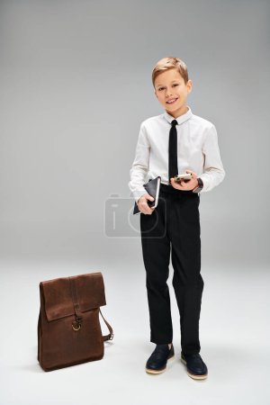 Preadolescent boy stands by briefcase in elegant attire.