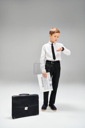 Guapo joven se pone de pie con confianza junto a un elegante maletín.
