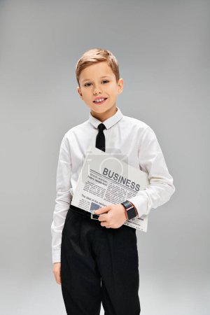 Niño con atuendo formal sosteniendo un periódico sobre un fondo gris.