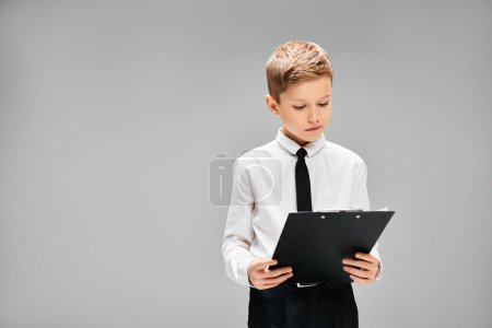 A preadolescent boy in white shirt and tie holds a black folder.