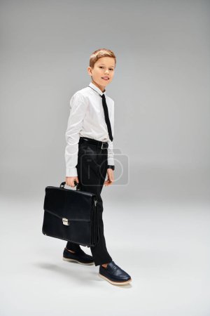 Preadolescent boy in suit, tie, holding briefcase, exuding confidence.