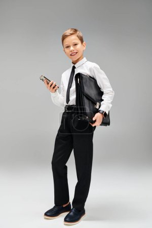 Niño preescolar con camisa y corbata, sosteniendo con confianza un teléfono celular.